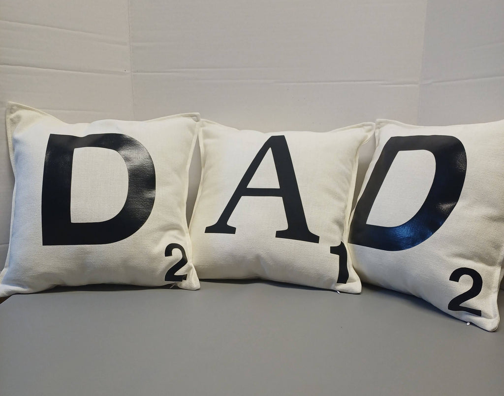 Three pillows with 'DAD' and numbers on a gray surface.