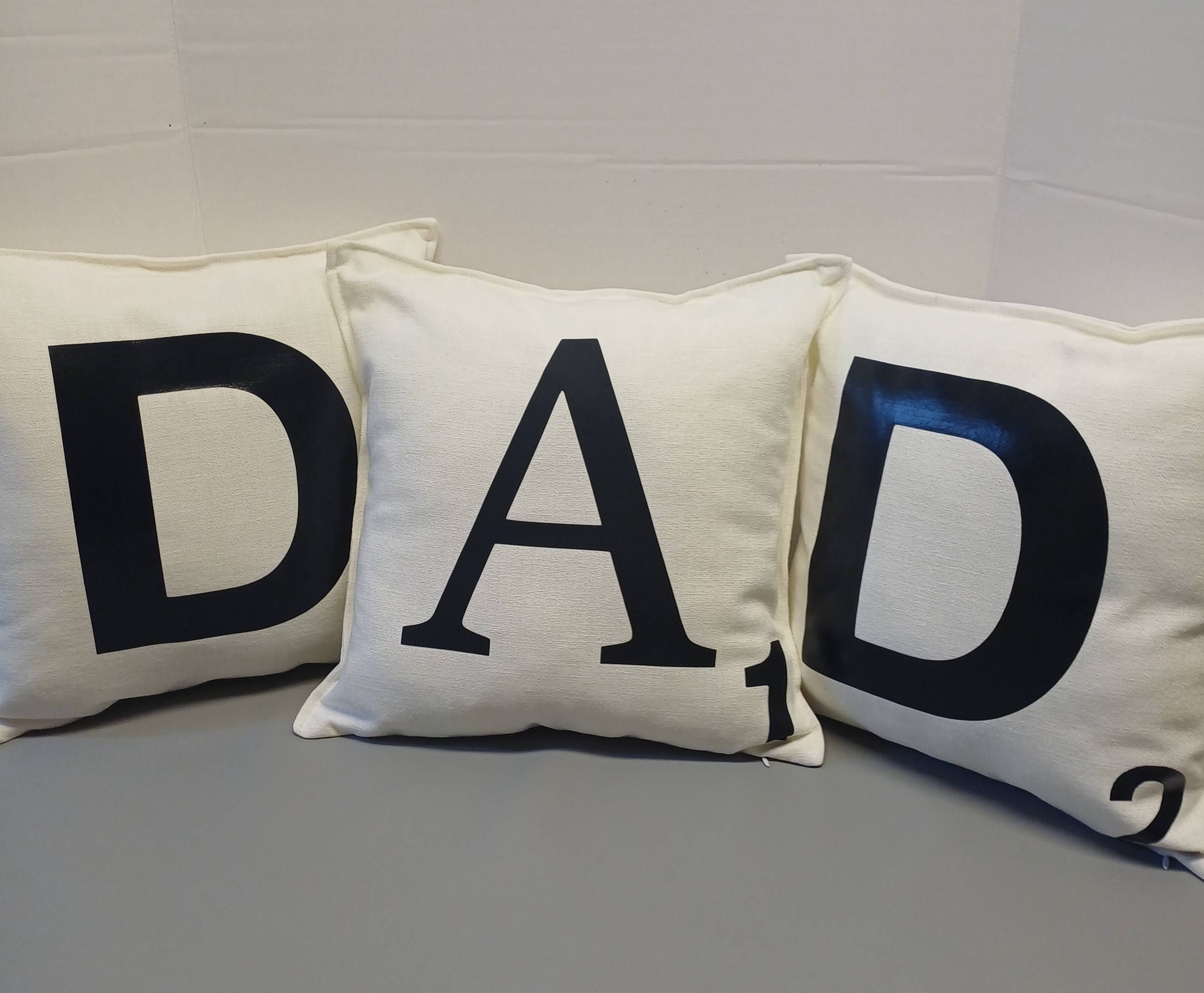 Three pillows with 'DAD' letters on a gray surface.